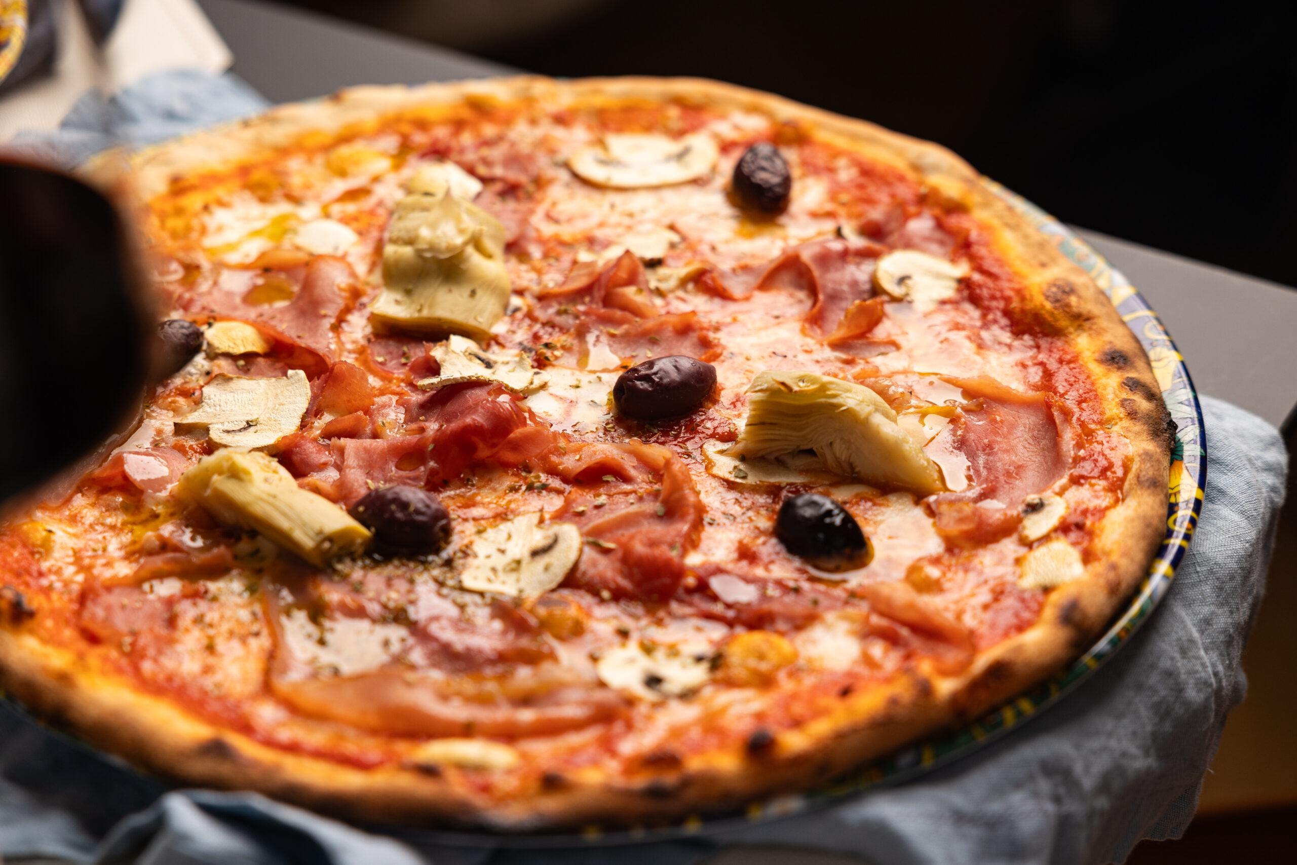 leckere Pizza mit Schinken, Artischocken und Oliven auf einem Teller im Restaurant Rossini in Wien