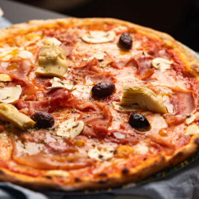 leckere Pizza mit Schinken, Artischocken und Oliven auf einem Teller im Restaurant Rossini in Wien